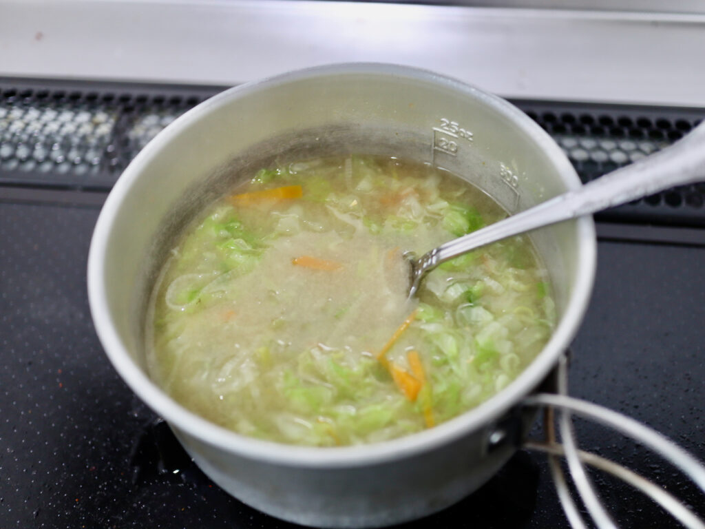 アルミクッカーの目盛りを見ながらスプーンで味噌を溶き入れる様子