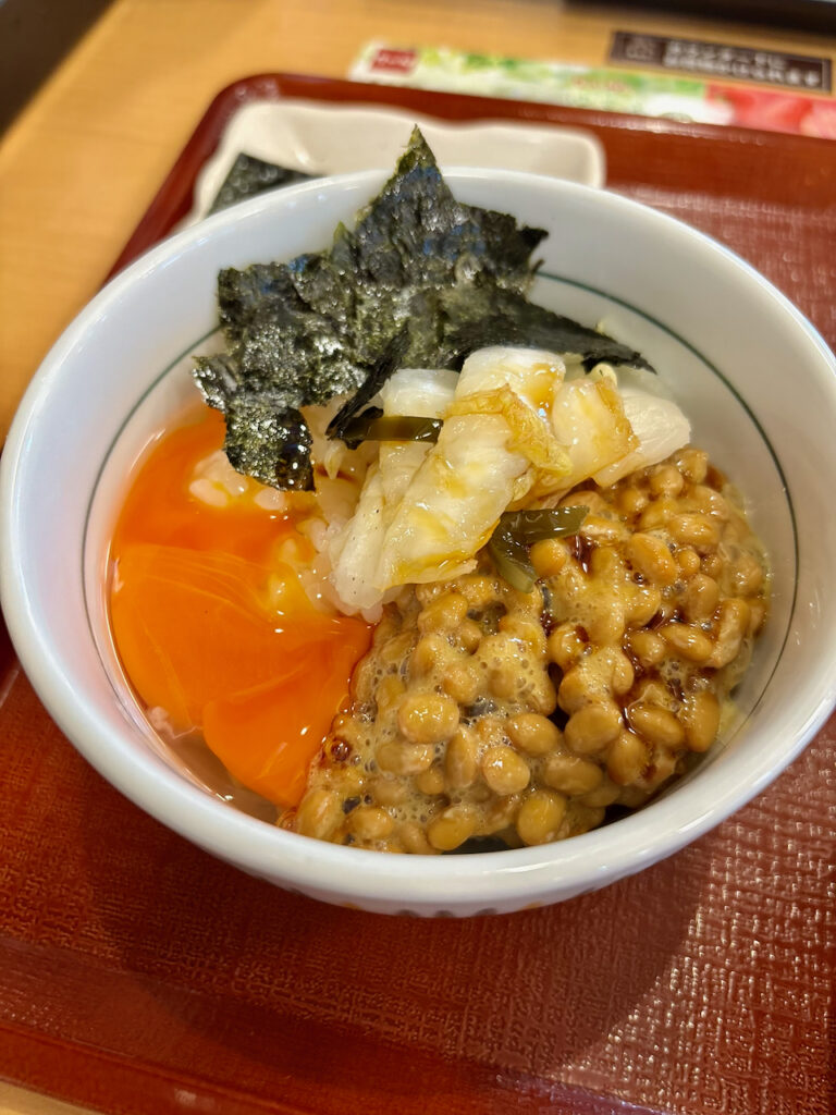 なか卯のご飯の上に、鮮やかなオレンジ色のこだわり卵、納豆、おしんこ、海苔を美しく盛り付けた特製アレンジ朝食どんぶりの写真